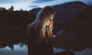 woman looking at phone beside body of water