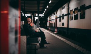 man in black jacket sitting on bench in train station