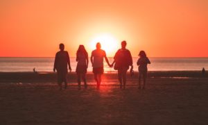 silhouette photo of five person walking on seashore during golden hour