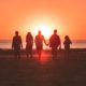 silhouette photo of five person walking on seashore during golden hour